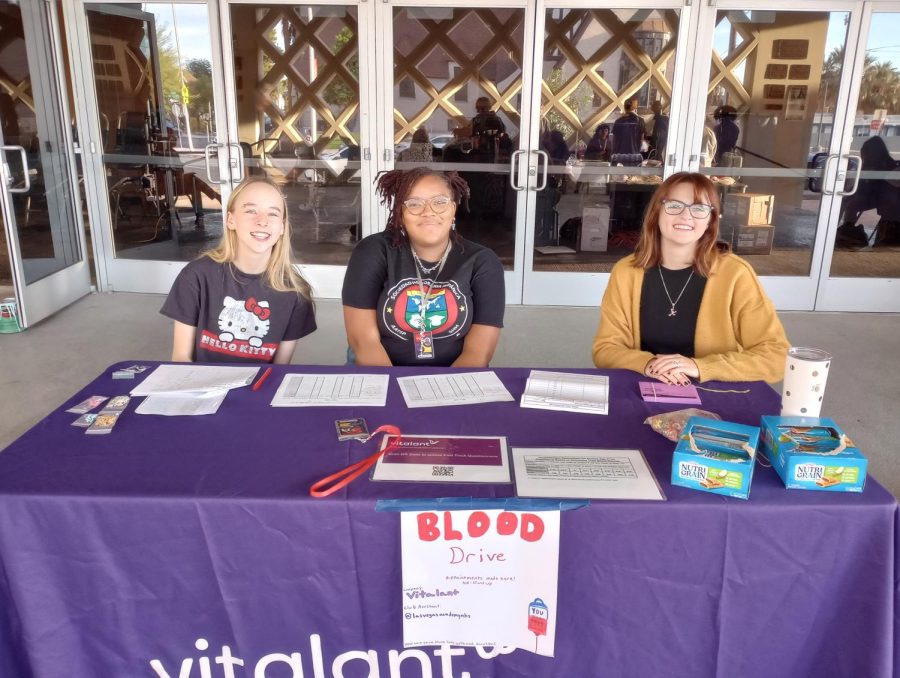 Three NHS Members at the blood drive sign-in table handing out snacks.