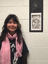 Visual Arts major, Cyenna Nash, smiles next to their artwork displayed in the halls of the Visual Arts building.