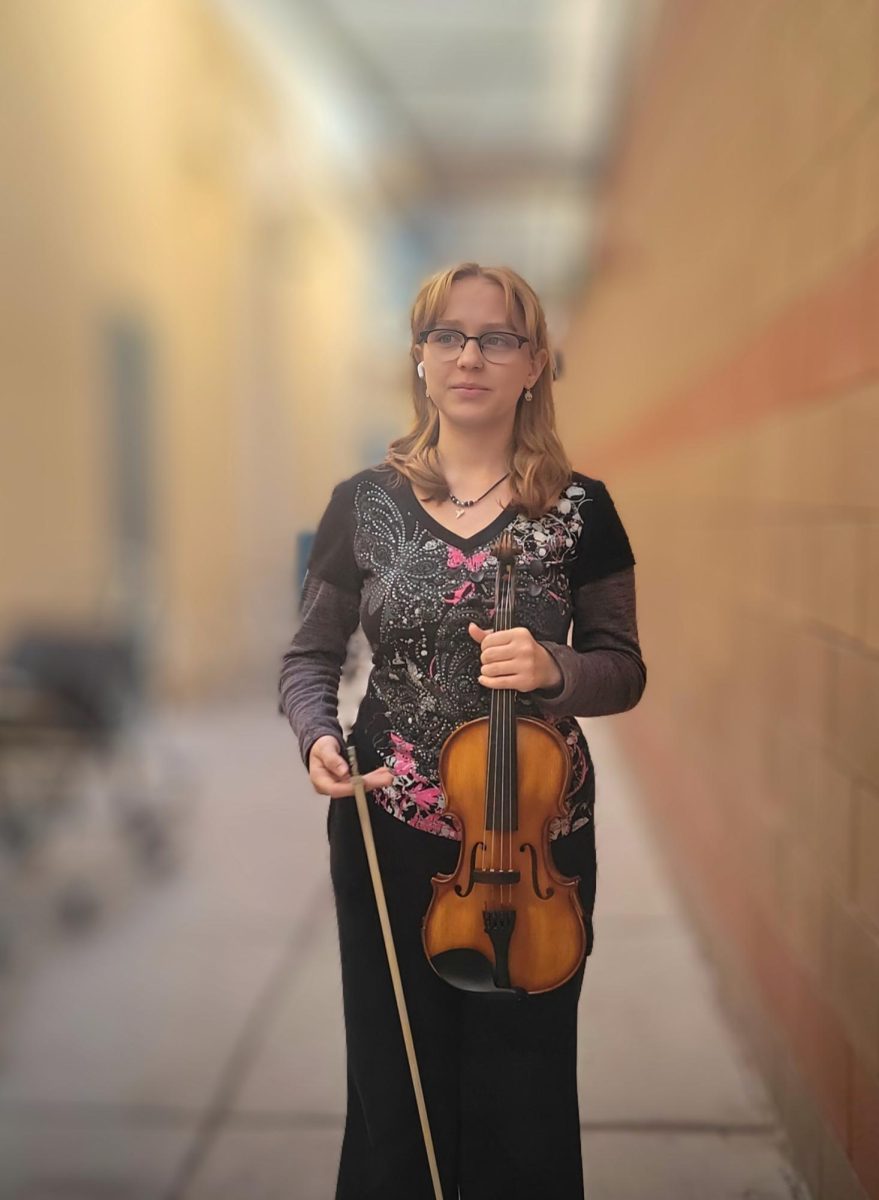 Jazmin Ellis poses with their viola outside the orchestra room.