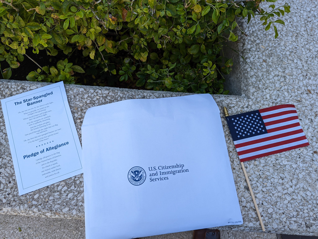 "Citizenship packet and oath, federal building, Downtown Los Angeles, California, USA" by gruntzooki is licensed under CC BY-SA 2.0. To view a copy of this license, visit https://creativecommons.org/licenses/by-sa/2.0/?ref=openverse.
