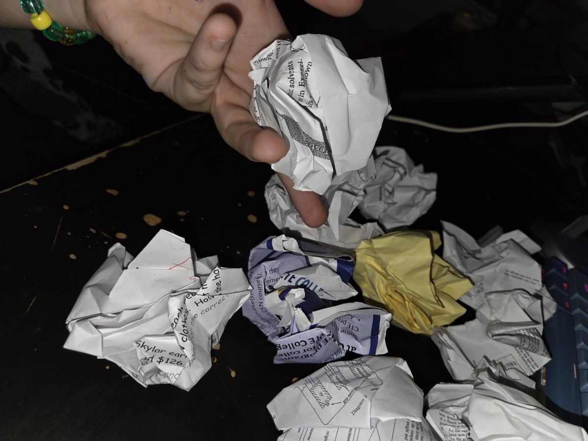 Hand tossing a crumpled paper into a pile full of school & collage papers all crumpled up next to each other.